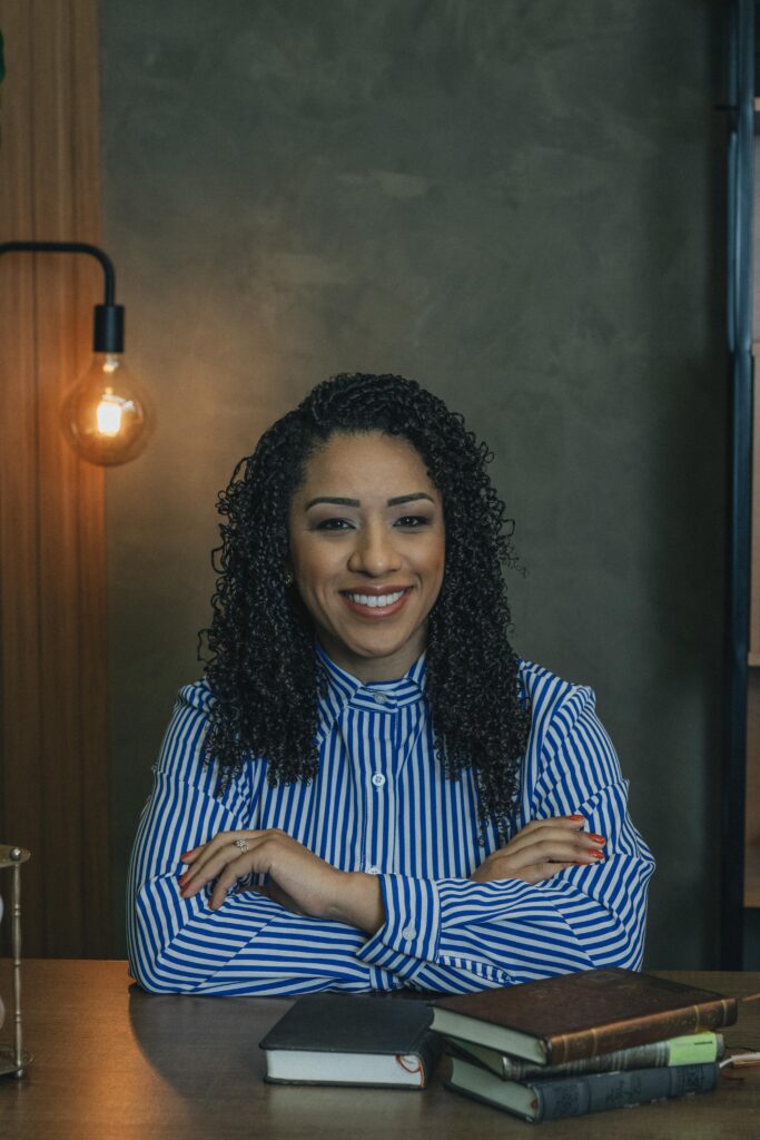 Confident woman sitting at desk with books, smiling warmly.
